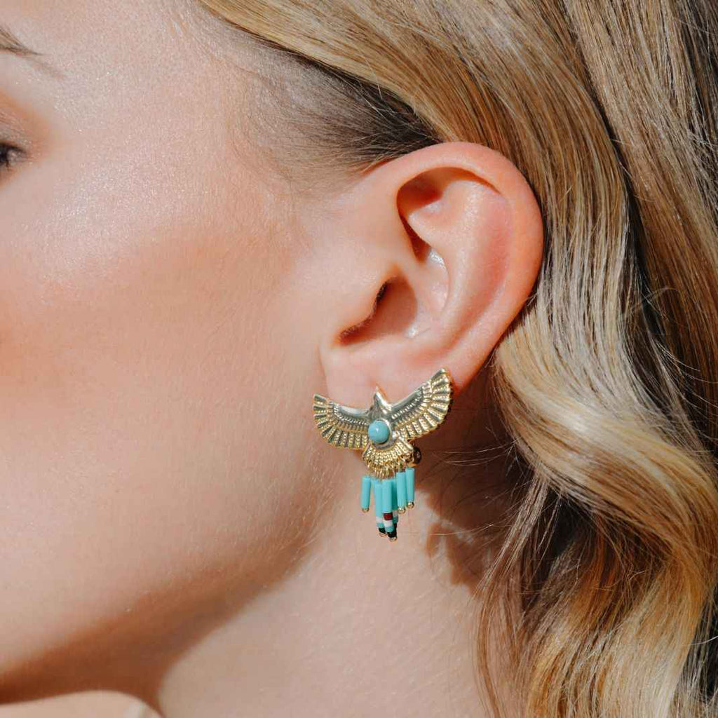 Close-up of an ear wearing a gold and turquoise earring with blonde hair.