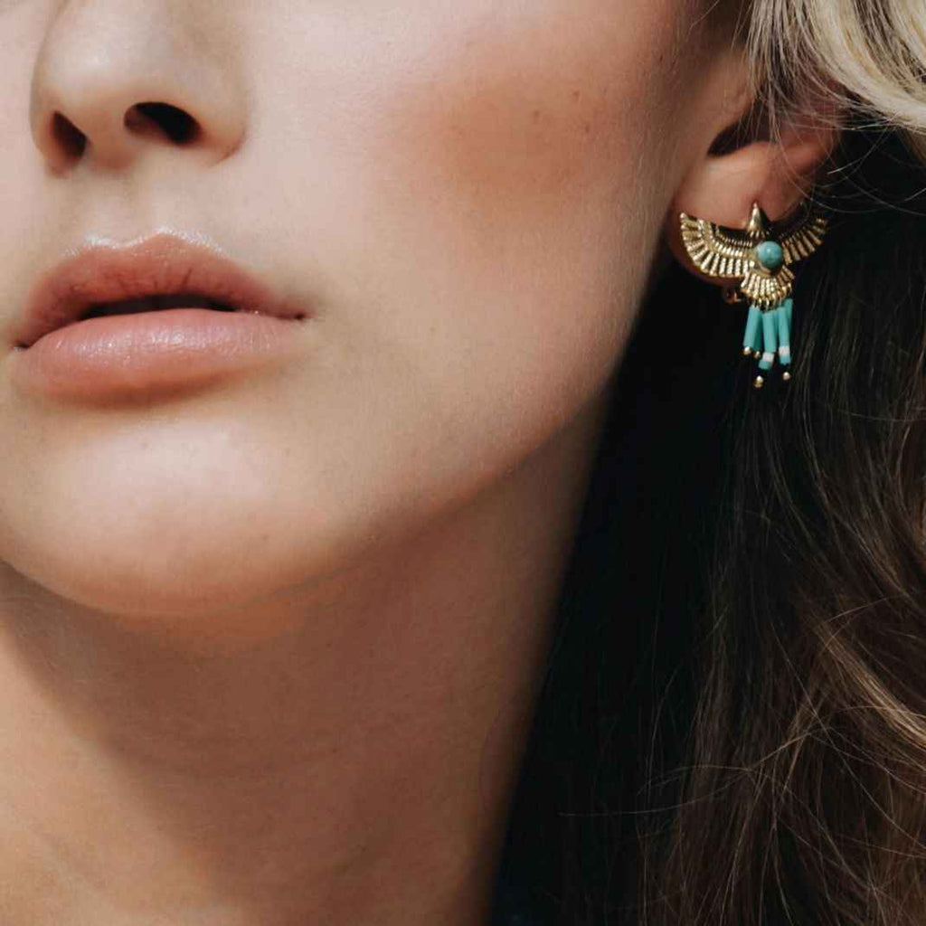 Close-up of a woman wearing an earring with turquoise stone and gold accents.