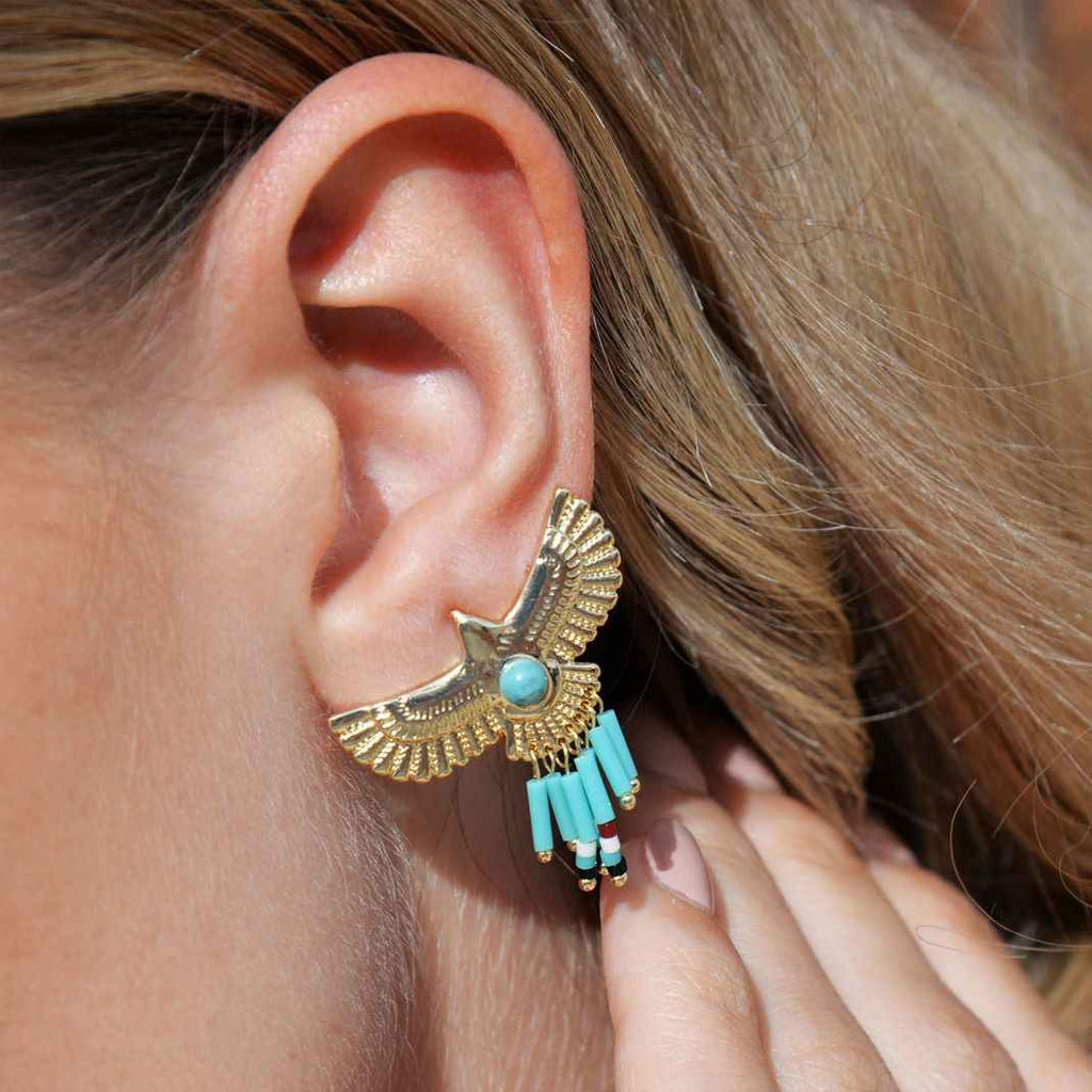 Close-up of an ear wearing a decorative gold and turquoise earring.