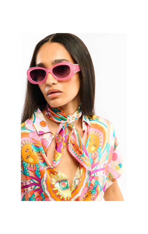 Woman wearing a colorful patterned shirt and scarf with pink sunglasses on a white background