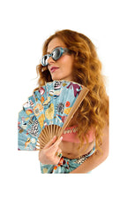 Woman holding a fan, wearing sunglasses and a colorful outfit on a white background