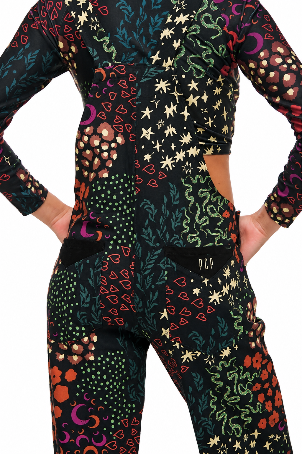 A long-sleeve crop top and matching pants set with a busy psychedelic print on a black base, featuring colorful snakes, stars, hearts, and floral motifs. The set is shown on a model from the back, with hands in pockets, against a plain white background.