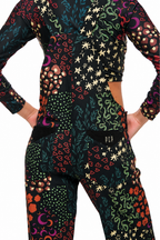A long-sleeve crop top and matching pants set with a busy psychedelic print on a black base, featuring colorful snakes, stars, hearts, and floral motifs. The set is shown on a model from the back, with hands in pockets, against a plain white background.