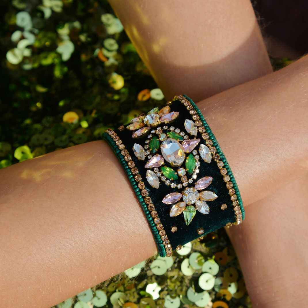 Decorative bracelet with gemstones on a wrist against a blurred green background