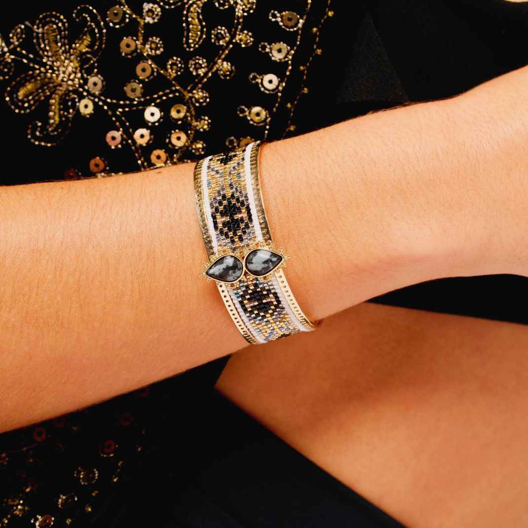 Close-up of a wrist wearing a decorative bracelet with gemstones on a black background.