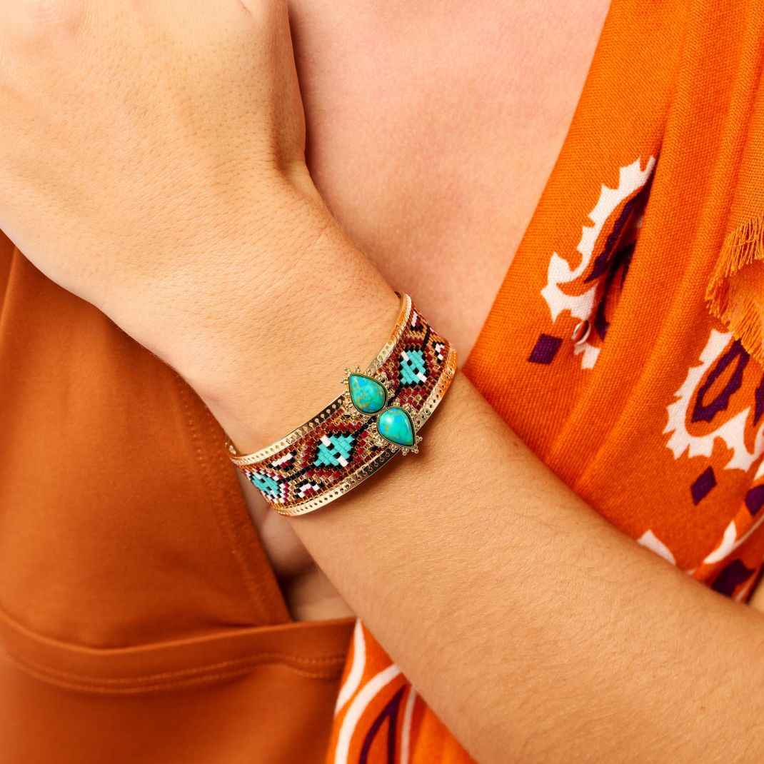Close-up of a person wearing a decorative bracelet with turquoise stones on an orange shirt.