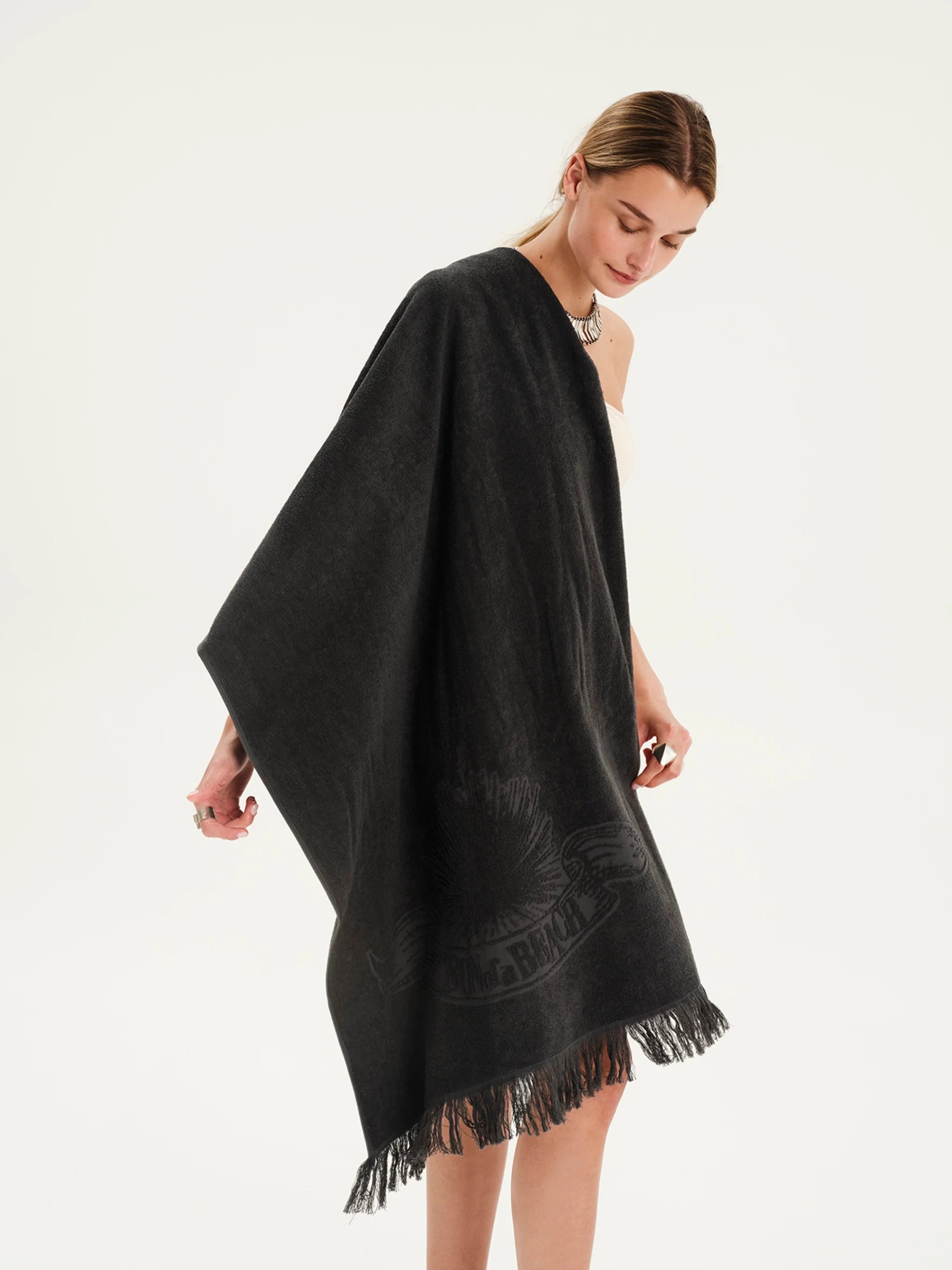 Woman wearing a black poncho with fringe details on a white background