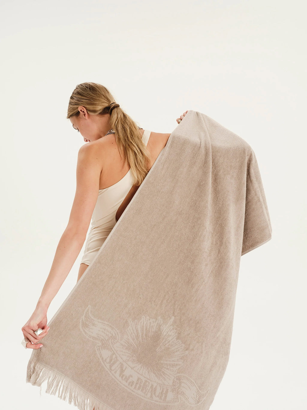 Woman holding a beige towel with a brand logo on a white background