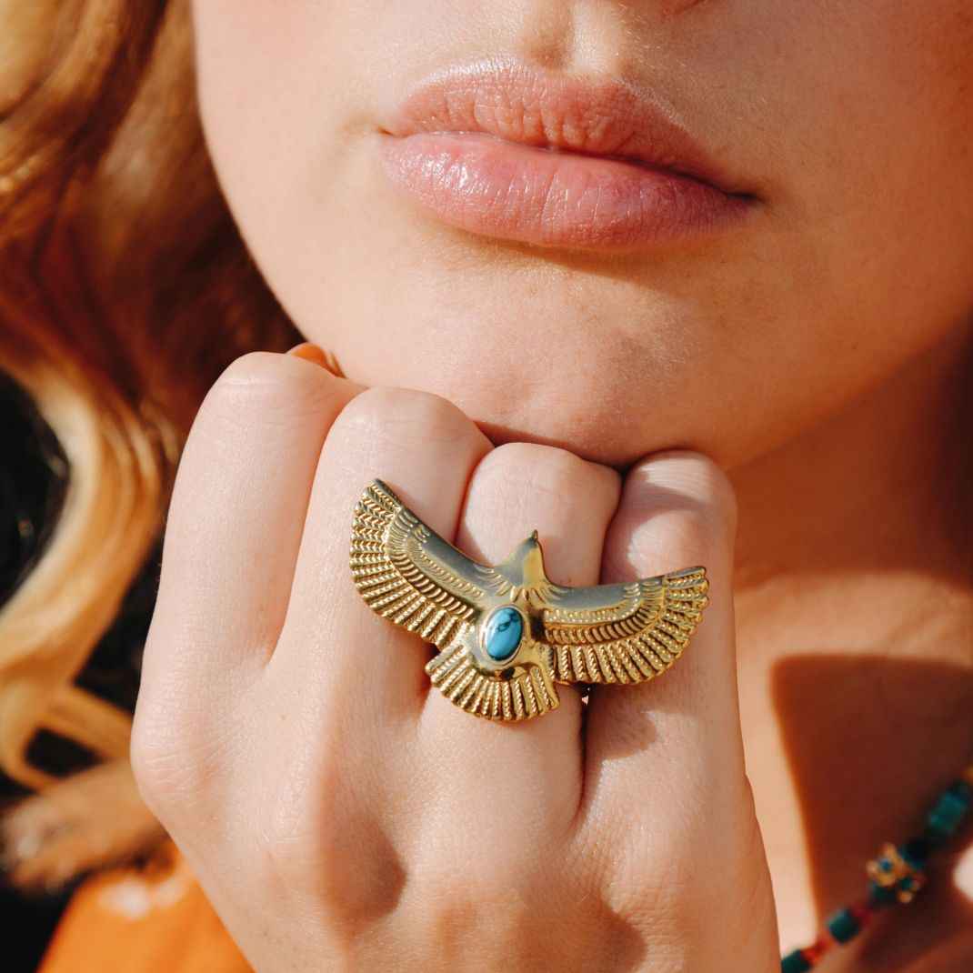 Close-up of a woman's hand wearing a gold ring with a blue stone, against a blurred background.
