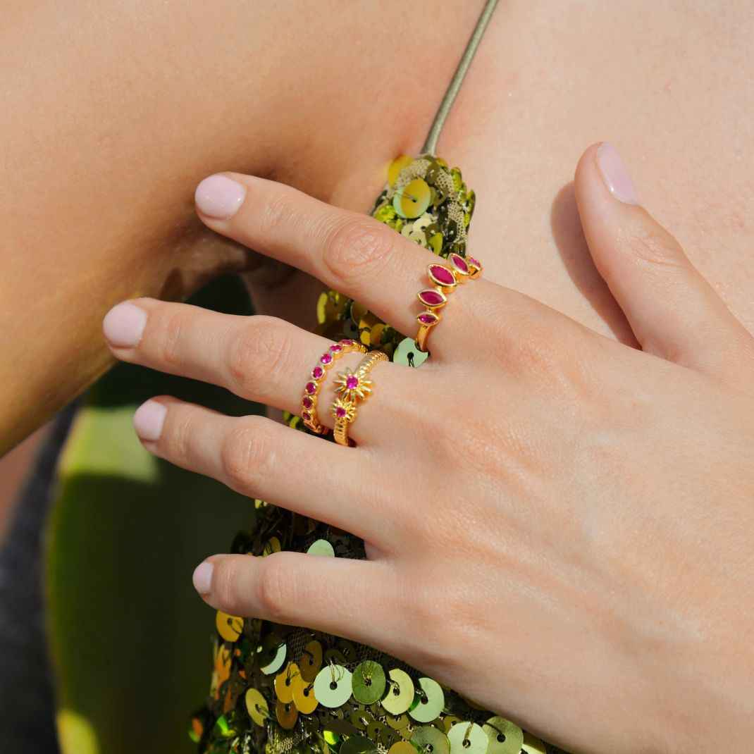 Close-up of a hand wearing two gold rings with gemstones on a sequined garment.