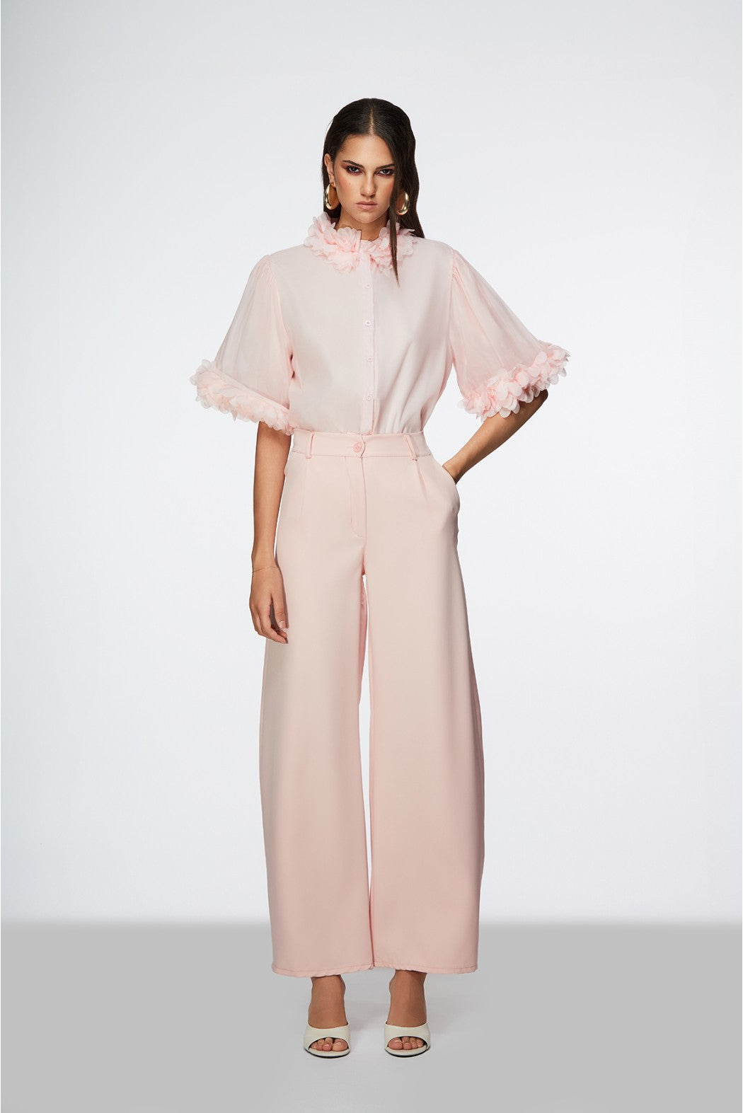 Woman wearing a light pink outfit with sheer sleeves on a white background