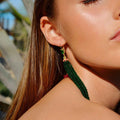 Close-up of a woman wearing green beaded earrings with a blurred outdoor background