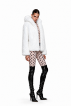 A model wearing a white faux fur jacket with a large plush collar, paired with pink patterned leggings and shiny black patent leather knee-high boots, shot against a solid white background.