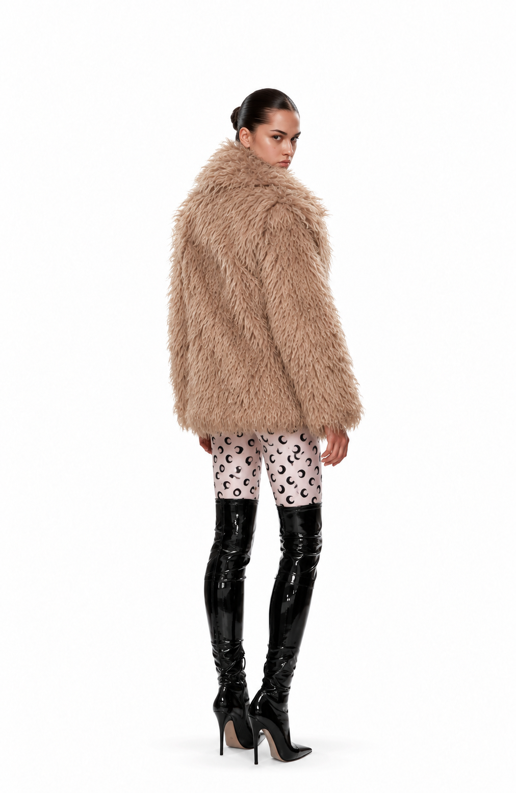 A model shown from the back wearing a voluminous, light brown shaggy faux fur coat, patterned pink and white leopard-print leggings, and black patent leather over-the-knee boots, against a solid white background.