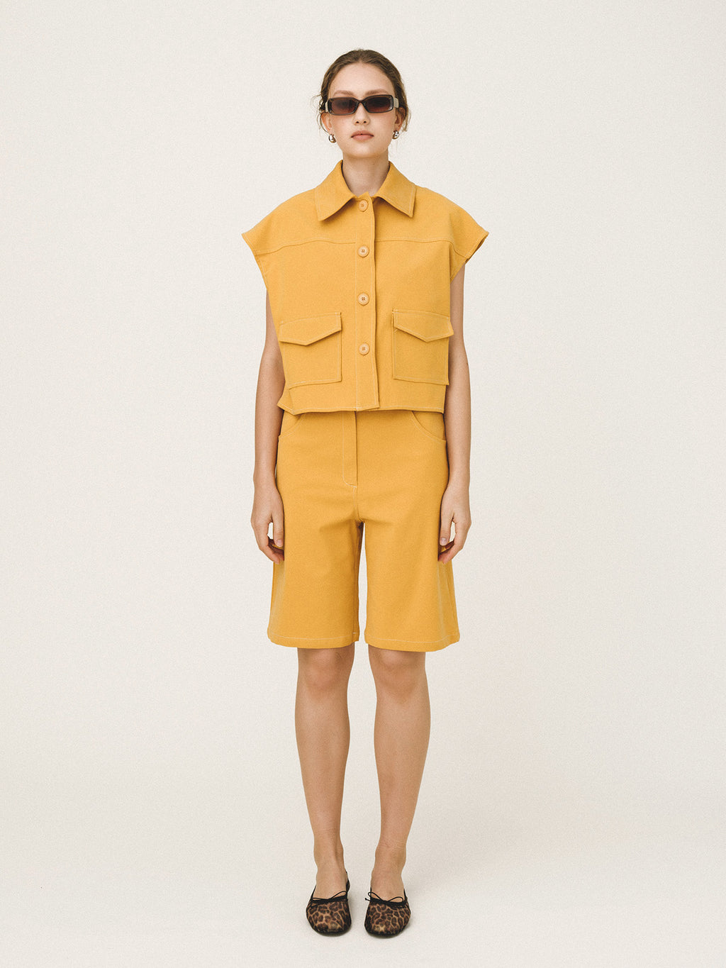 Person wearing a mustard yellow sleeveless top and shorts set on a white background