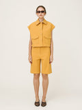 Person wearing a mustard yellow sleeveless top and shorts set on a white background