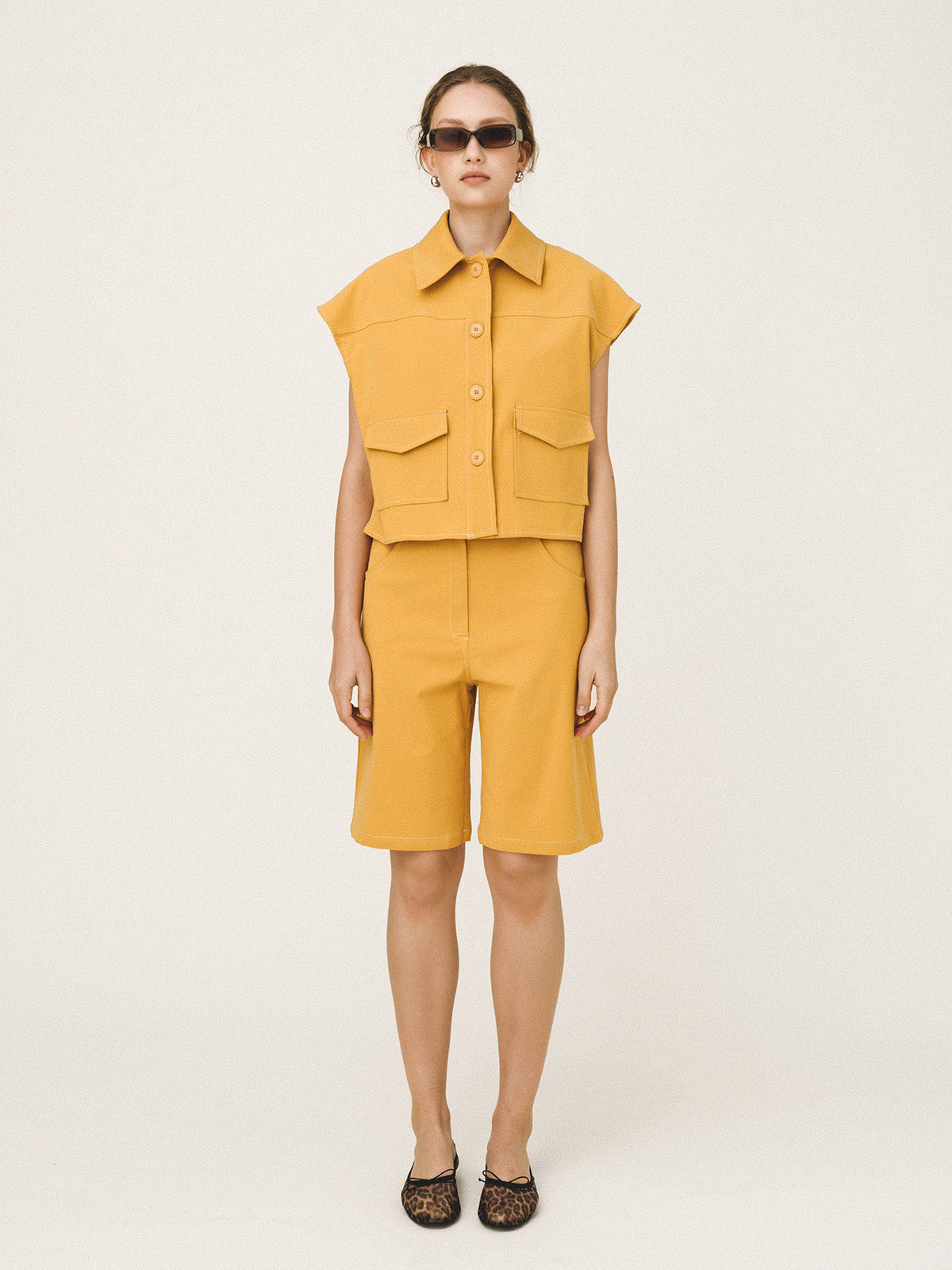 Person wearing a mustard yellow sleeveless top and shorts set on a white background