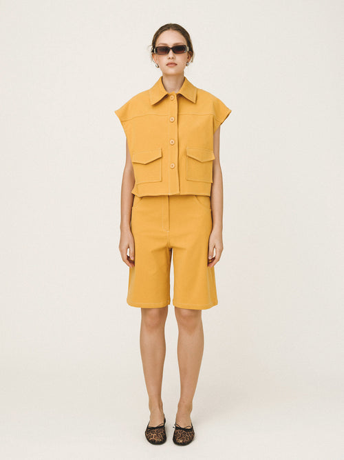 Person wearing a mustard yellow sleeveless top and shorts set on a white background