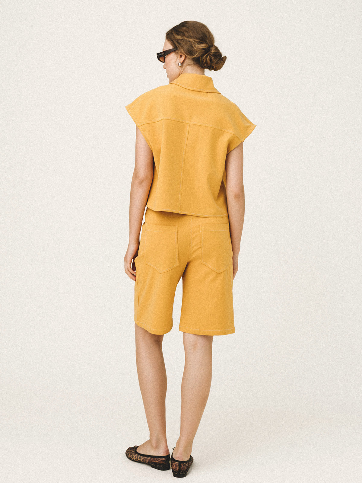Woman wearing a yellow sleeveless top and shorts on a white background