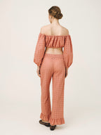 A woman shown from the back wearing a matching two-piece set with an off-the-shoulder long-sleeve crop top and wide-leg pants, both in a dusty rose pink color with a small geometric pattern. She is standing against a plain light background.