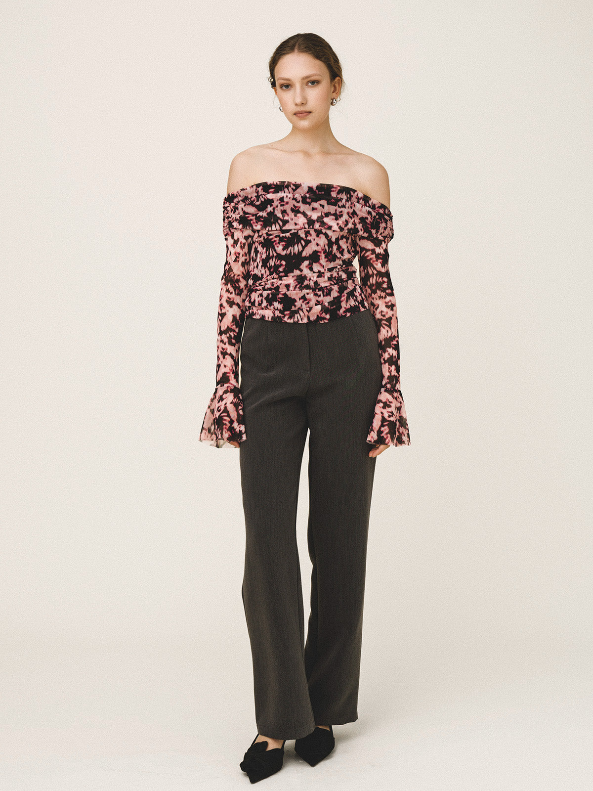 Woman wearing a floral off-shoulder top and black pants on a white background