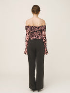 Woman wearing a floral off-shoulder top and black pants on a white background