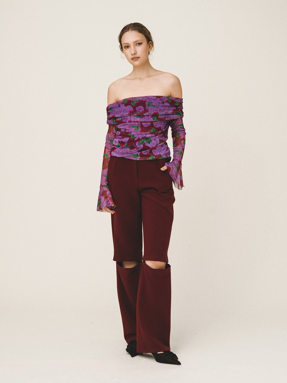 Woman wearing a purple floral off-shoulder top and burgundy pants on a white background