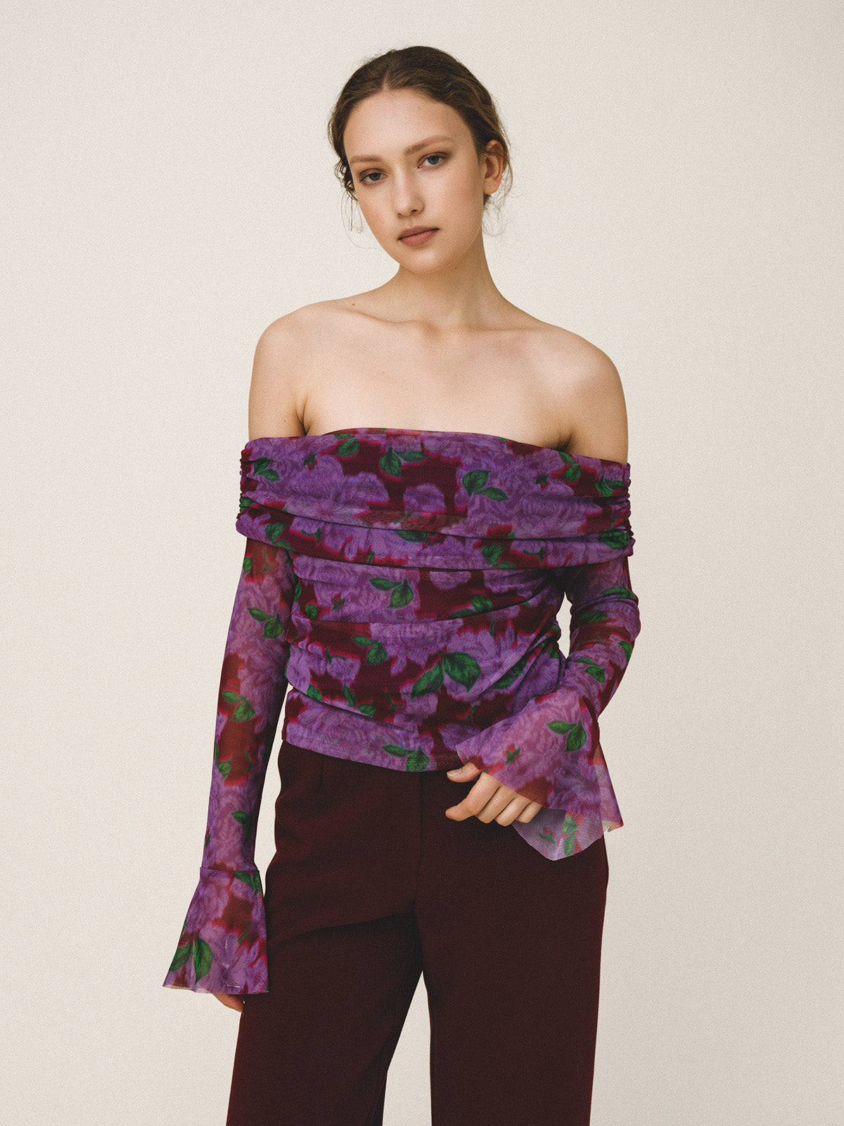 Woman wearing a purple floral off-shoulder top and dark pants on a beige background