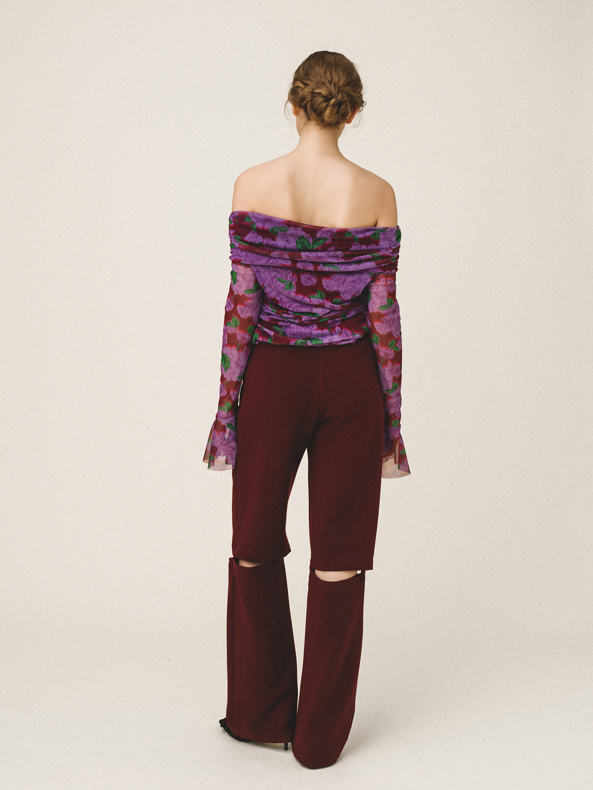 Woman wearing a purple floral off-shoulder top and burgundy pants on a white background