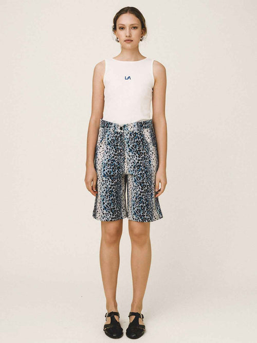 Woman wearing a white sleeveless top and patterned shorts on a plain background