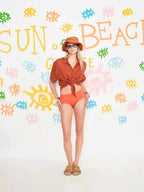 Woman in orange outfit standing against a colorful 'Sun Beach' background