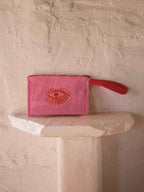 Pink pouch with a red handle on a white pedestal against a textured beige wall.