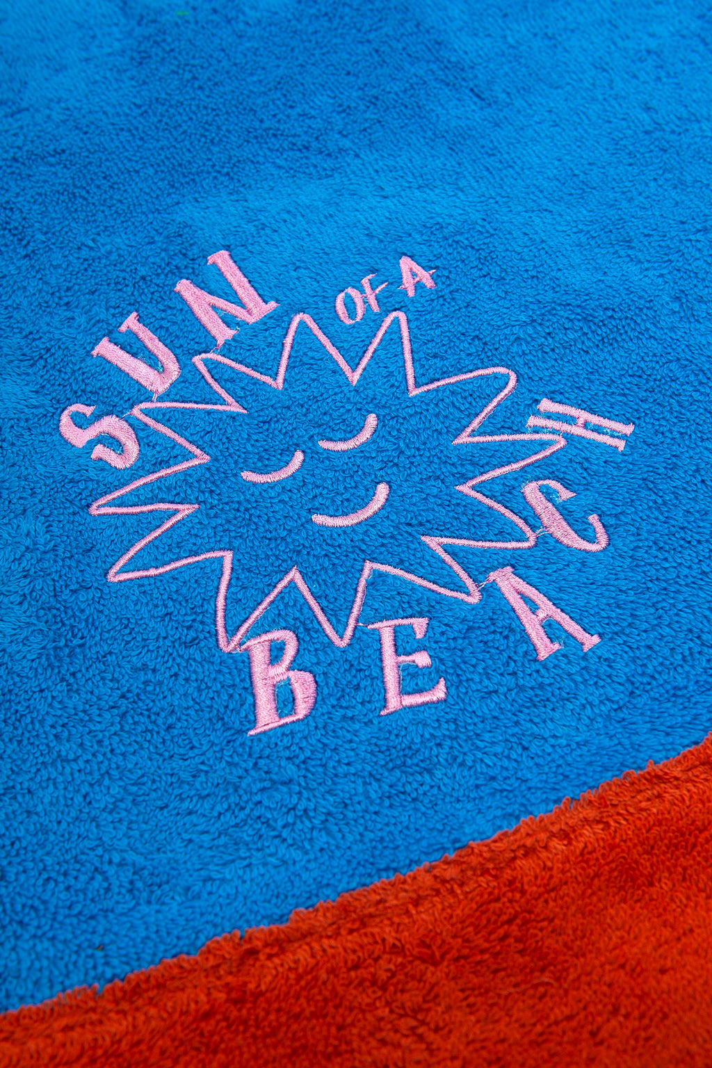 Blue towel with pink text and sun design, featuring the phrase 'Sun of a Beach'.