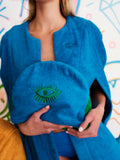 Person wearing a blue robe with green embroidered eye design, holding a green pillow.