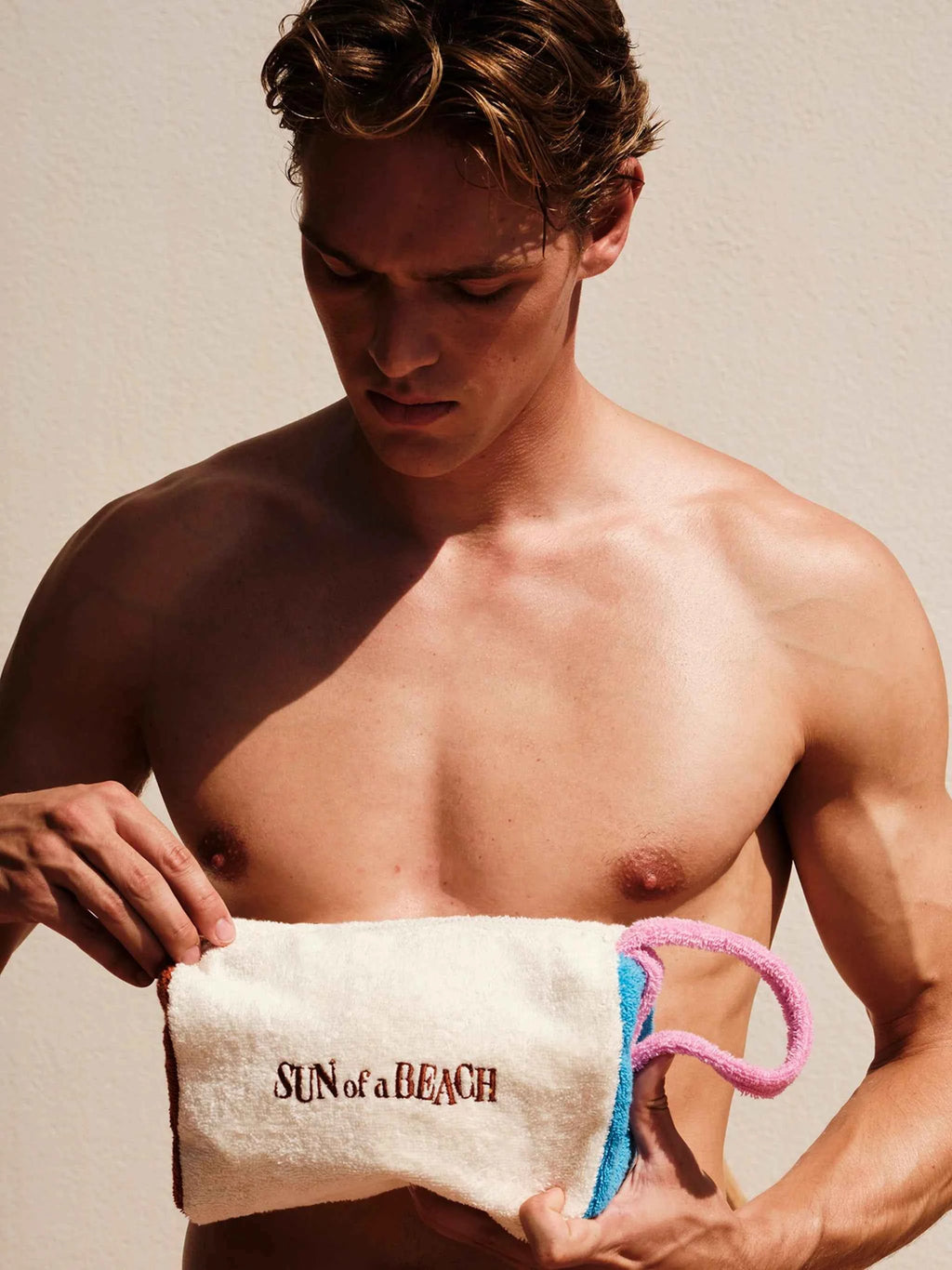 Man holding a towel with 'Sun of a Beach' text against a neutral background
