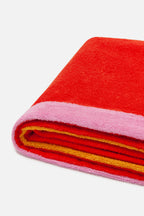 Folded red and pink towel with yellow trim on a white background