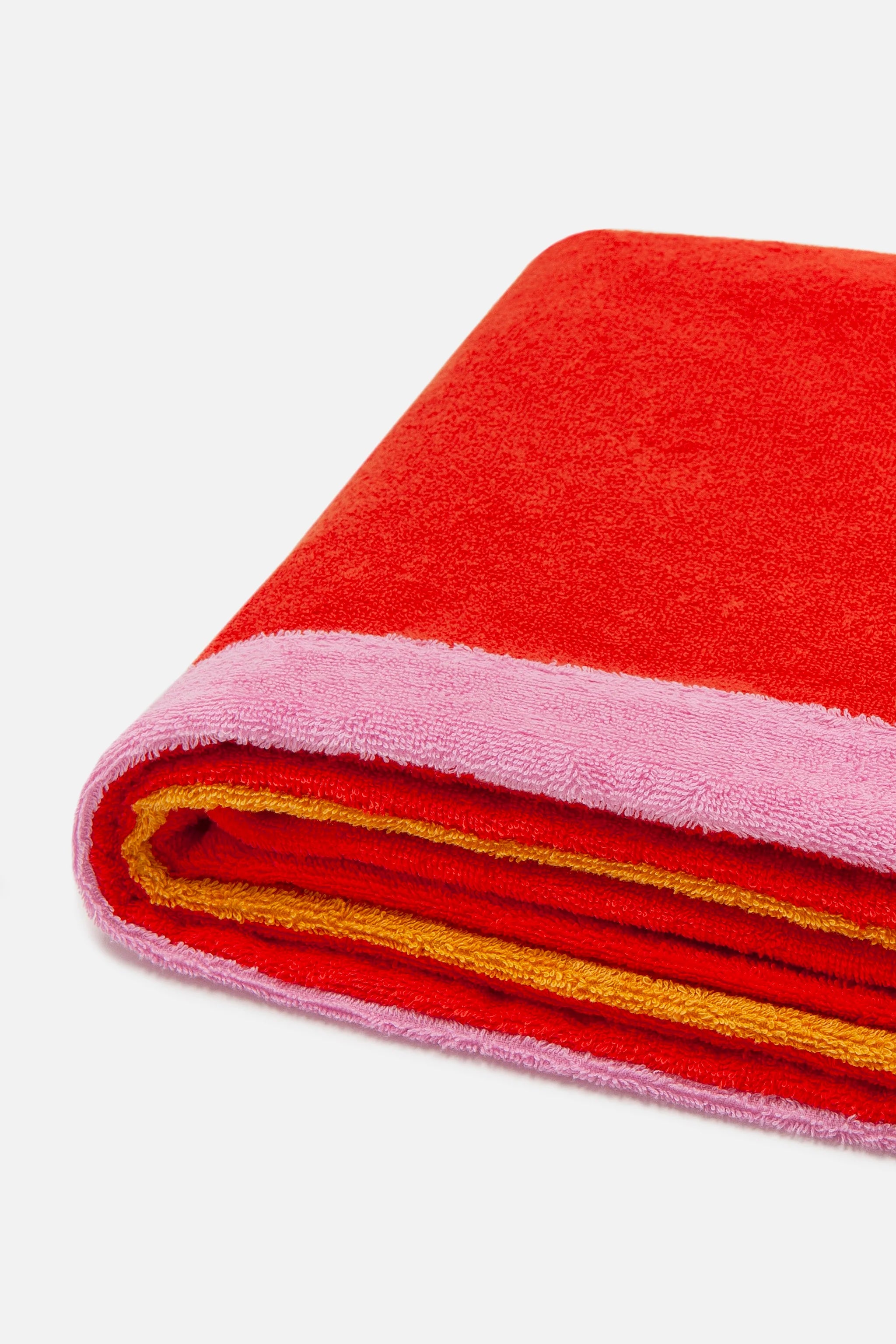 Folded red and pink towel with yellow trim on a white background