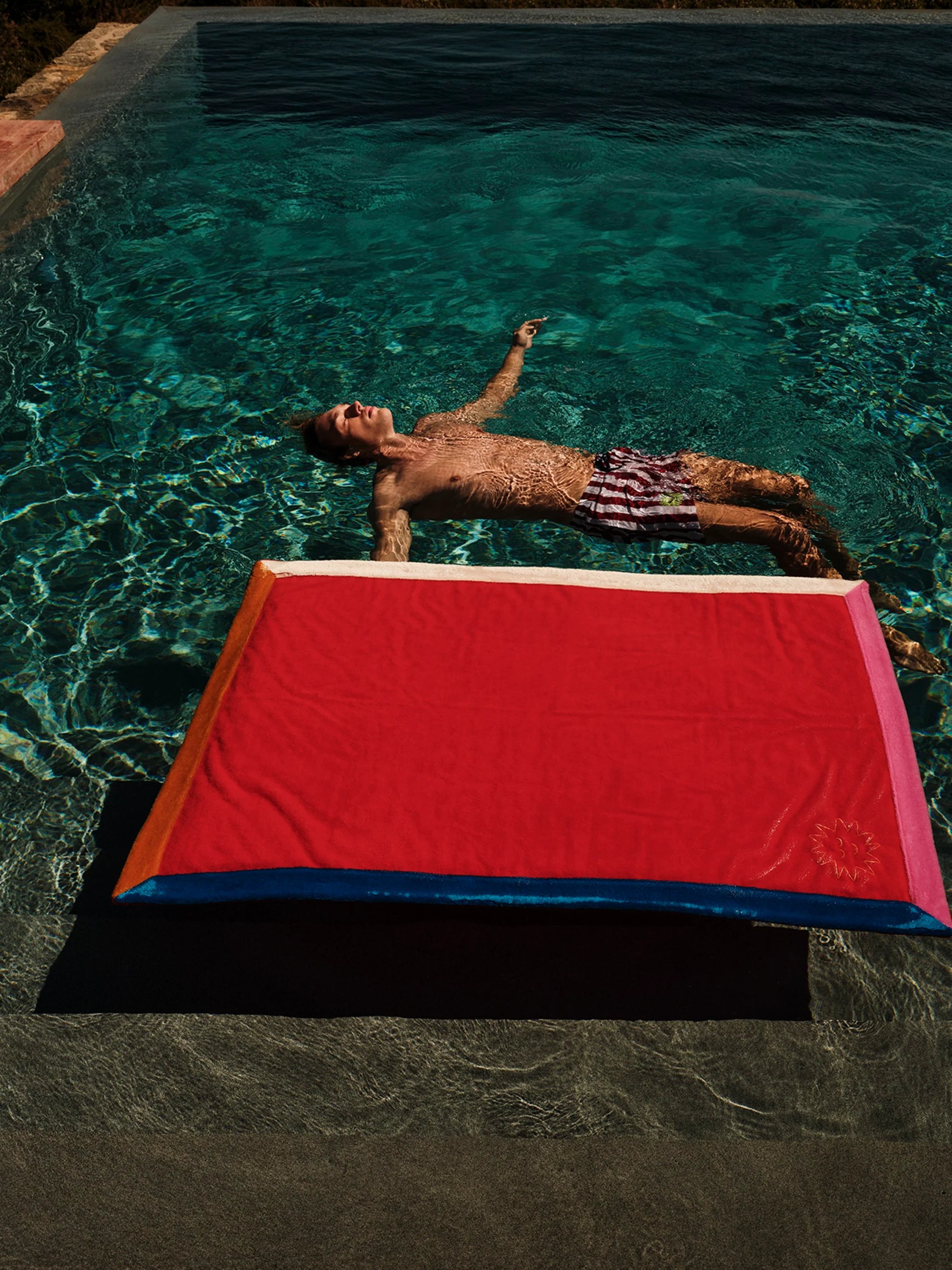 Person lying on a red and blue mat above a pool