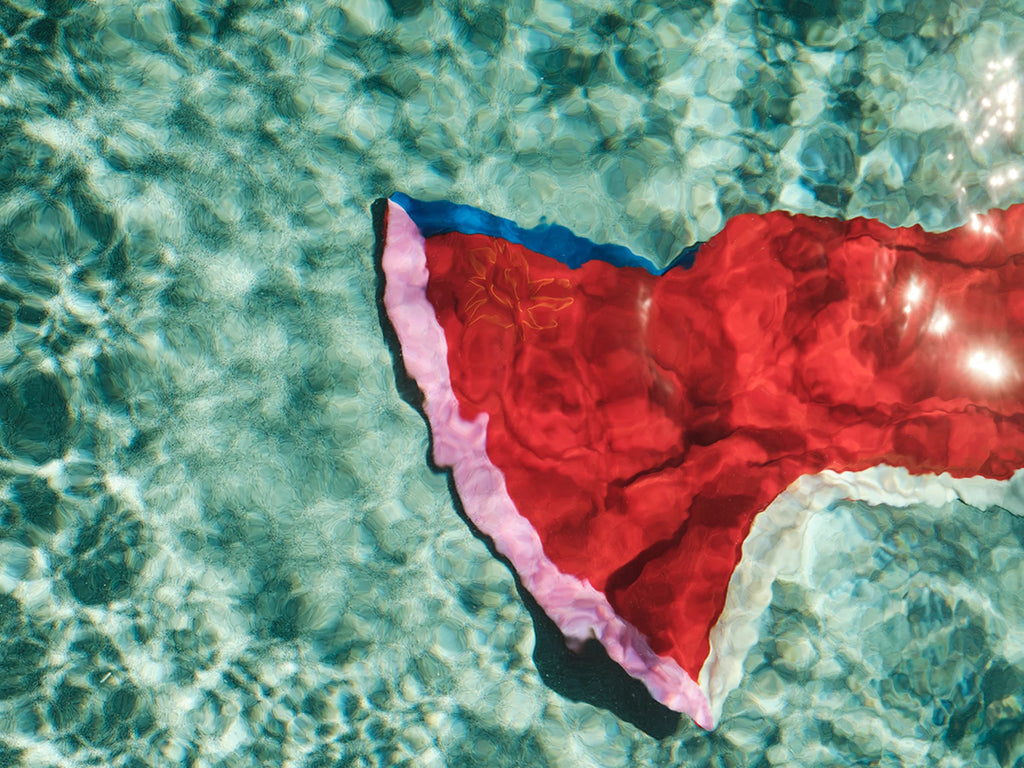 Red fabric with blue trim floating on clear water