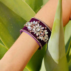 Purple bracelet with decorative stones on a wrist against a green leafy background