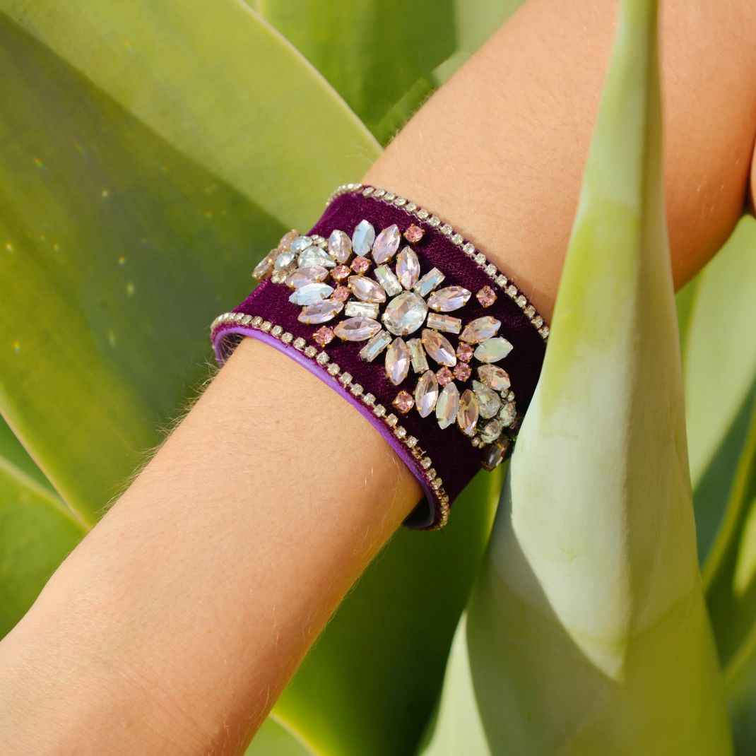 Purple bracelet with decorative stones on a wrist against a green leafy background