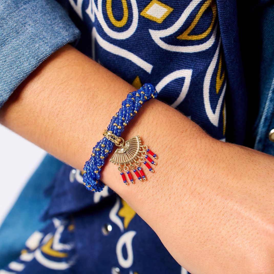 Close-up of a wrist wearing a blue beaded bracelet with red accents, against a blue patterned background.