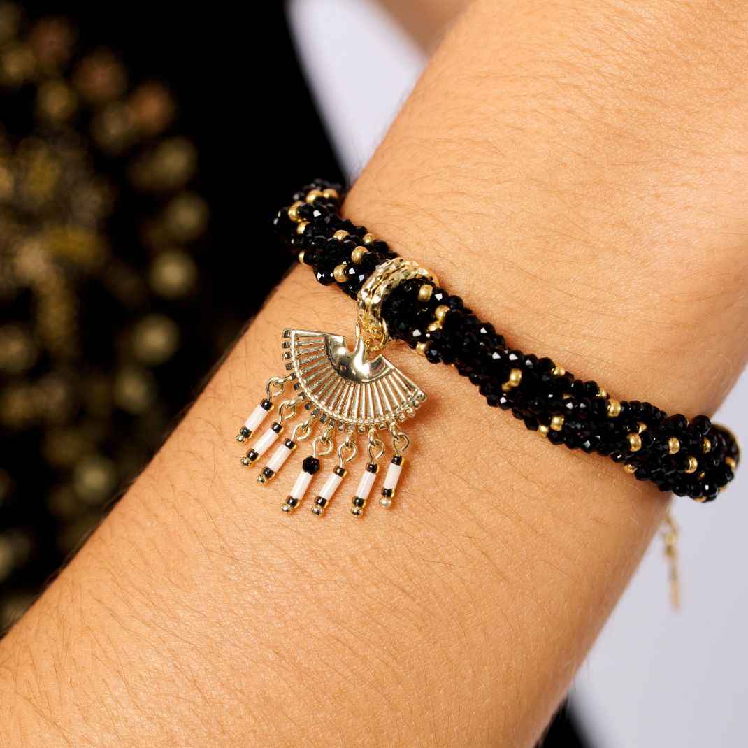 Black beaded bracelet with gold charm on a wrist against a blurred background