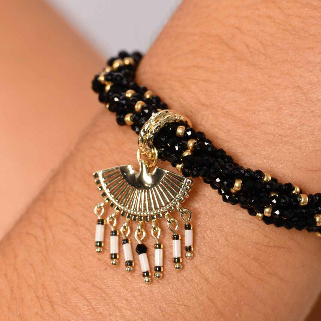 Black beaded bracelet with gold and white charm on a wrist
