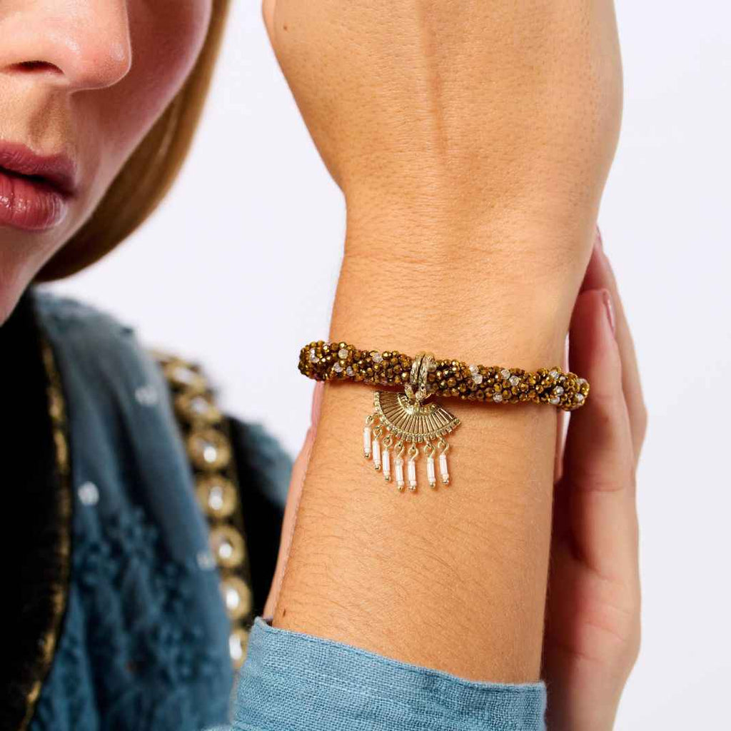 Close-up of a person wearing a gold bracelet with a decorative clasp on a plain background