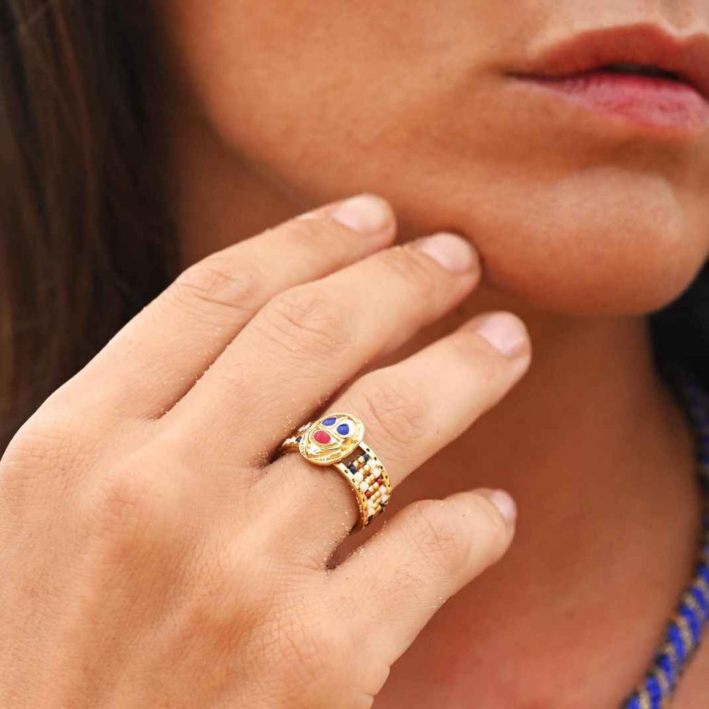 Close-up of a hand wearing a gold ring with colorful gemstones, blurred background