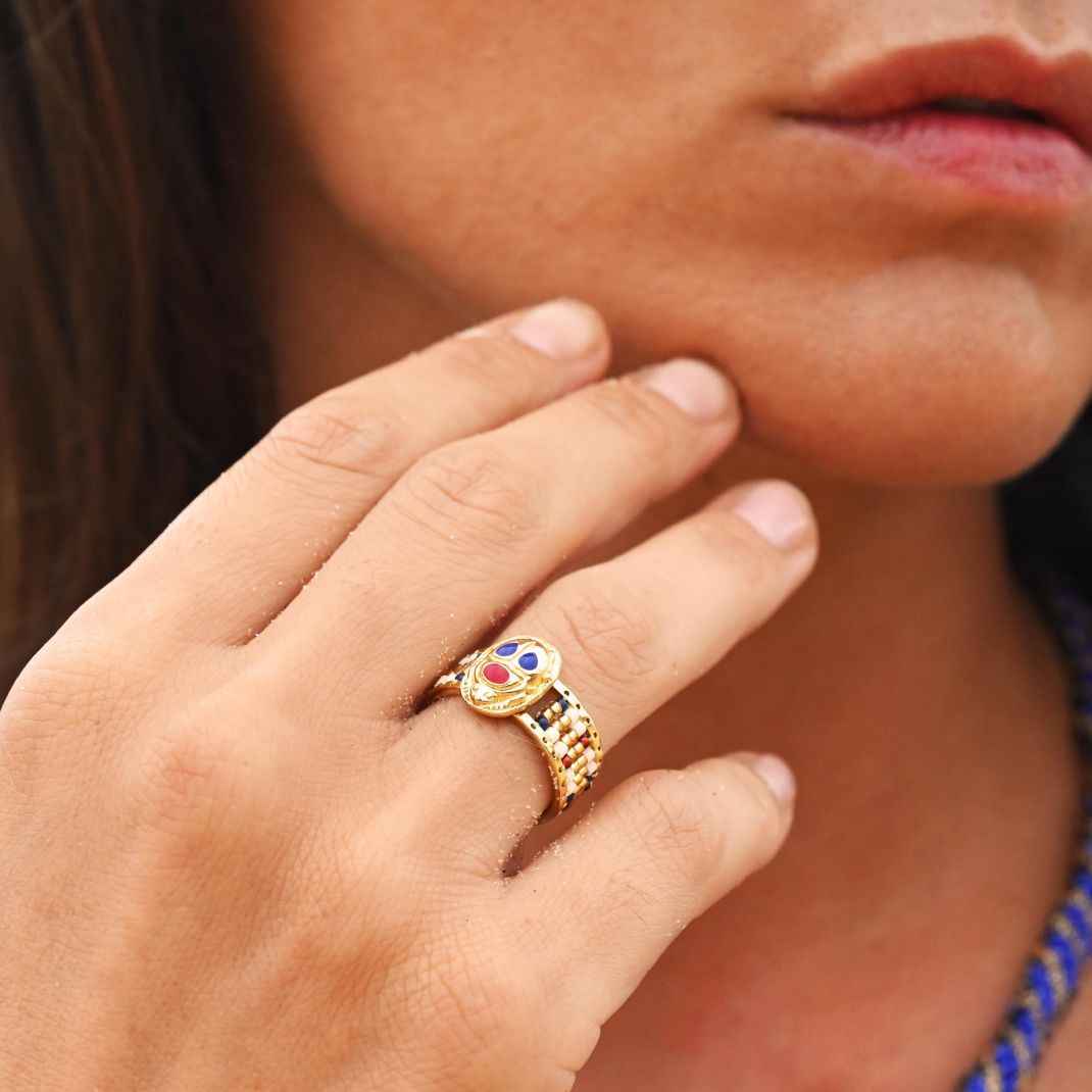 Close-up of a hand wearing a gold ring with colorful gemstones, blurred background