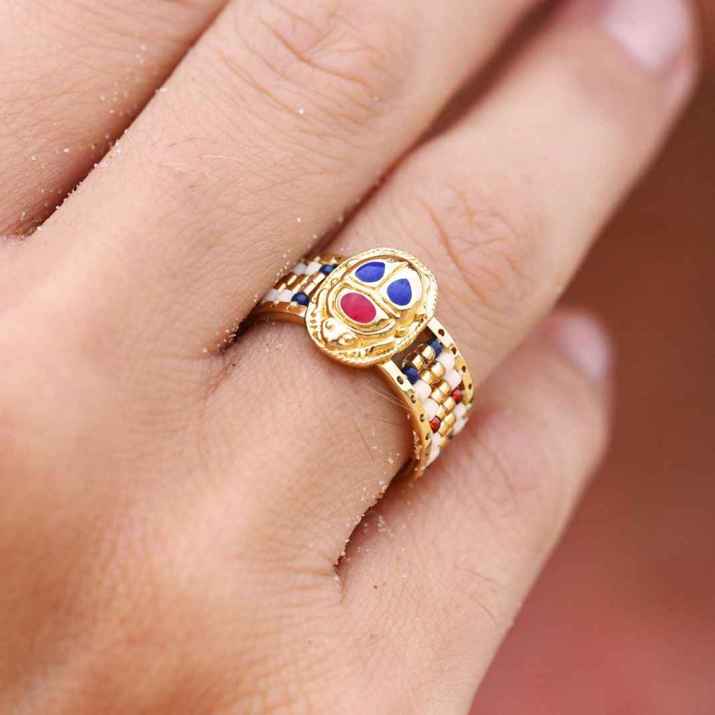 Gold ring with colorful gemstones on a finger against a blurred background