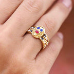 Gold ring with colorful gemstones on a finger against a blurred background