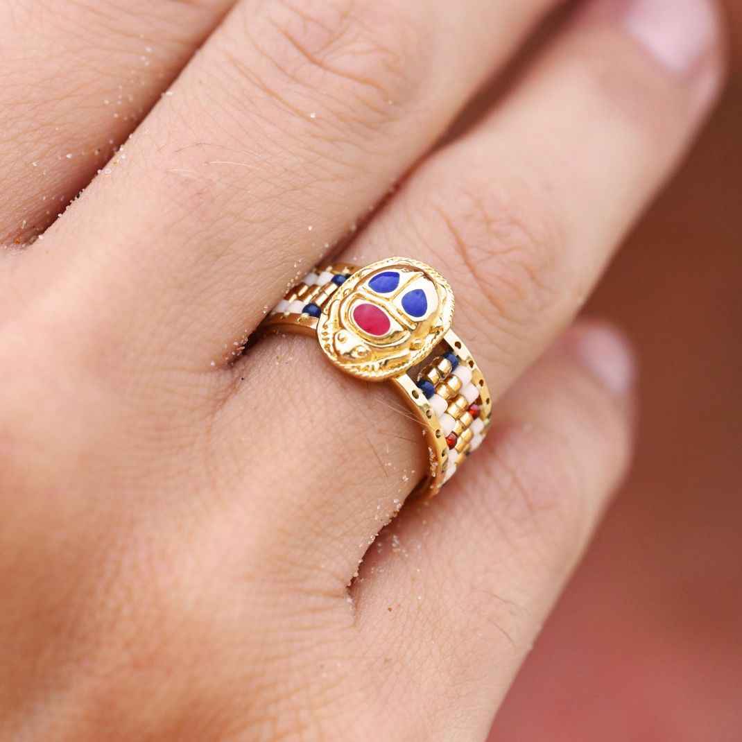 Gold ring with colorful gemstones on a finger against a blurred background